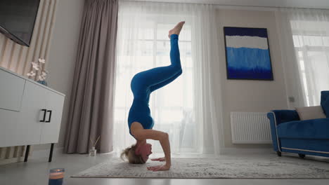 A-sporty-beautiful-woman-performs-a-stand-on-her-head-and-hands-at-home.-On-the-carpet-of-his-own-apartment.-Balance-exercises